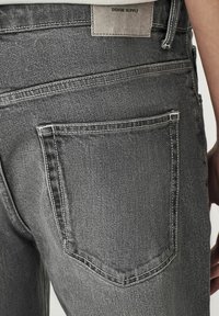 Graue Denim-Jeans mit kontrastierendem weißen Nähten, ausgestattet mit zwei Gesäßtaschen und einem Lederetikett mit der Aufschrift "DENIM SUPPLY" am Bund.