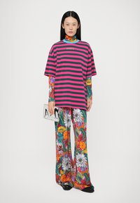 Ριγέ ροζ και πράσινο oversized μπλουζάκι, παντελόνι με λουλούδια σε έντονες αποχρώσεις και μεταλλική τσάντα, φορεμένο με μαύρα παπούτσια.