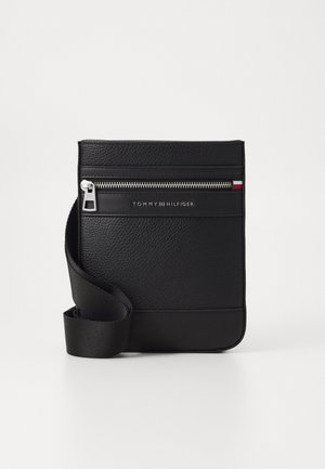 Sac bandoulière noir texturé avec bandoulière en tissu ajustable, fermeture éclair argentée et logo Tommy Hilfiger avec détail drapeau sur le devant.