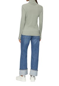 Jasnoszary sweter z golfem zestawiony z luźnymi niebieskimi dżinsami, z wywiniętymi mankietami i srebrnymi trampkami na platformie. Gładka tekstura i dopasowany krój.