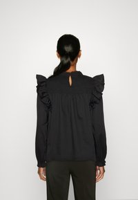 Blusa nera con maniche arricciate, pannello posteriore arricciato e dettaglio a chiave sulla scollatura. Tessuto morbido con maniche lunghe e polsini arricciati.