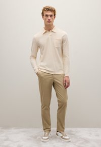 Helle beige Langarm-Polohemd mit einer Brusttasche, kombiniert mit hellen, tanfarbenen Hosen und cremigen Sneakers mit beigen Akzenten.