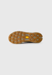 Sål af en vandresko med dybe orange gummilugger og et centralt gult Vibram-logo på en lysegrå baggrund.