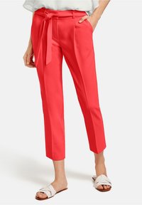 Pantalons corail lumineux avec une ceinture nouée à la taille, design court et texture de tissu lisse. Associés à des sandales plates blanches à lanières.