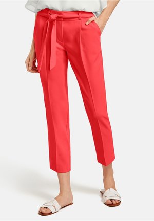 Pantalons corail lumineux avec une ceinture nouée à la taille, design court et texture de tissu lisse. Associés à des sandales plates blanches à lanières.