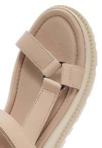 Sandal en cuir beige avec deux brides, présentant un accent métallique circulaire et une semelle texturée pour une meilleure adhérence. Fini lisse et semelle intérieure matelassée.