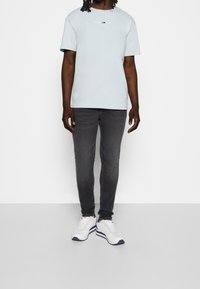 Ljusblå kortärmad t-shirt med "TOMMY JEANS"-logotyp, i kombination med mörkgrå slim-fit jeans och vita sneakers med marinblå och röda detaljer.