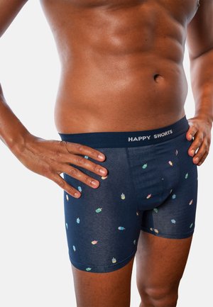 Man with toned torso wearing navy blue boxer briefs patterned with colorful ice cream popsicles, hands resting on hips.