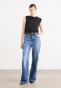 Svart ermeløs topp med drapert design, parret med lyseblå høyt midje jeans. Jeansene har rett passform og subtil falming. Svart hæler.