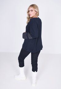 Marineblauwe gebreide trui met gestructureerde grijze accenten op de mouwen, gecombineerd met donkere spijkerbroek en witte combat-achtige laarzen.