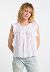 Top bianco senza maniche con bordo arricciato sulle spalle, caratterizzato da un motivo a righe verticali testurizzate e un corpetto ampio e arricciato. Abbinate a jeans chiari.