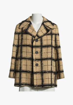 Manteau beige avec un grand motif à carreaux noirs, large col à revers et trois boutons noirs à l'avant sur un mannequin blanc.