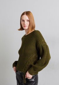 Olivgrüner gestrickter Pullover mit strukturiertem Muster und weiten Ärmeln. Verfügt über ein seitliches Kabeldesign und eine lockere Passform.