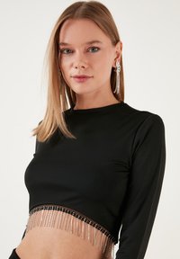 Čierne dlhé rukávy crop top s priehľadným lemom zdobeným strieborným reťazovým třásním. Hladká tkanina s priliehavým strihom.