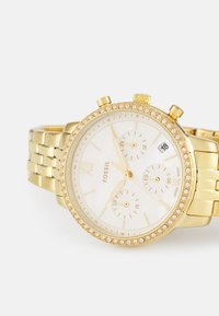Goldfarbene Fossil-Uhr mit einem strukturierten weißen Zifferblatt, drei Hilfszifferblättern und Kristallakzenten auf der Lünette. Verfügt über ein Metallgliederarmband und eine Datumsanzeige.