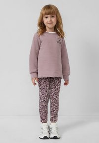 Liliowy sweatshirt z napisem "Nie śnij serca mojego", w zestawieniu z legginsami w kwiatowy wzór w purpurowe i białe. Białe sneakersy dopełniają stylizację.