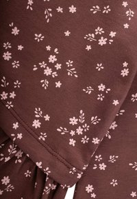 Rjavo blago s cvetličnim vzorcem v svetlo roza barvi. Vzorec vključuje majhne cvetove in liste, razpršene po teksturi.