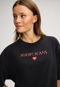 Zwart T-shirt van katoen met korte mouwen, met een roze opdruk waarop "JOOP!JEANS" en een hartsymbool staan.