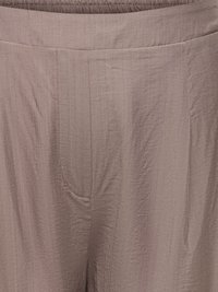 Close-up of beige textured fabric pants with elastic waistband and visible seam details on the front.