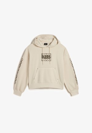 Beige lyhyt huppari, jossa on kiristysnauha huppuna, etutasku ja monimutkaiset mustat kuviot rinnassa ja hihoissa. Pehmeä kangas.