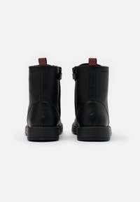 Bottines noires en cuir avec une finition lisse, des tirettes texturées rouges et noires, et une semelle en caoutchouc empilée.