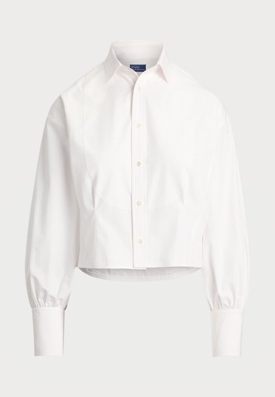 Λευκό κοντομάνικο πουκάμισο με κουμπιά φτιαγμένο από βαμβάκι. Διαθέτει μυτερό γιακά, μακριά φουσκωτά μανίκια και διακριτές καμπύλες ραφές. Κλασικός σχεδιασμός.