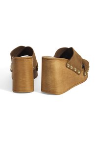 Sandales compensées marron avec un talon en bois, présentant une tige en daim, un dos ouvert et des clous décoratifs le long du côté.
