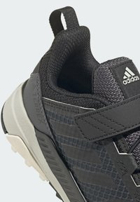 Černá sportovní bota s texturovaným síťovaným svrškem, obsahující suchý zip, polstrovaný límec a světlou šedou gumovou podrážku.