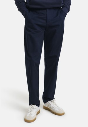 Navy blue trousers made from lightweight fabric, featuring a relaxed fit and side pockets, worn with white sneakers.