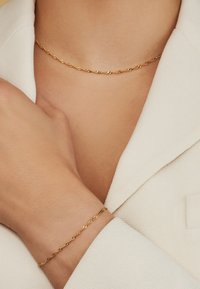 Collier et bracelet en chaîne torsadée dorée, présentant un design texturé et une finition lisse, portés sur un fond en tissu clair.