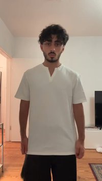 White short-sleeve shirt with a V-neck and minimal texture. Straight fit, smooth fabric, worn with dark pants, in a simple interior setting.