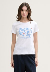 Hvit bomull T-skjorte med blå blomsterdesign og teksten "BLÅ ER DIN LYKKEFARGE" i blått. Korte ermer og rund hals.