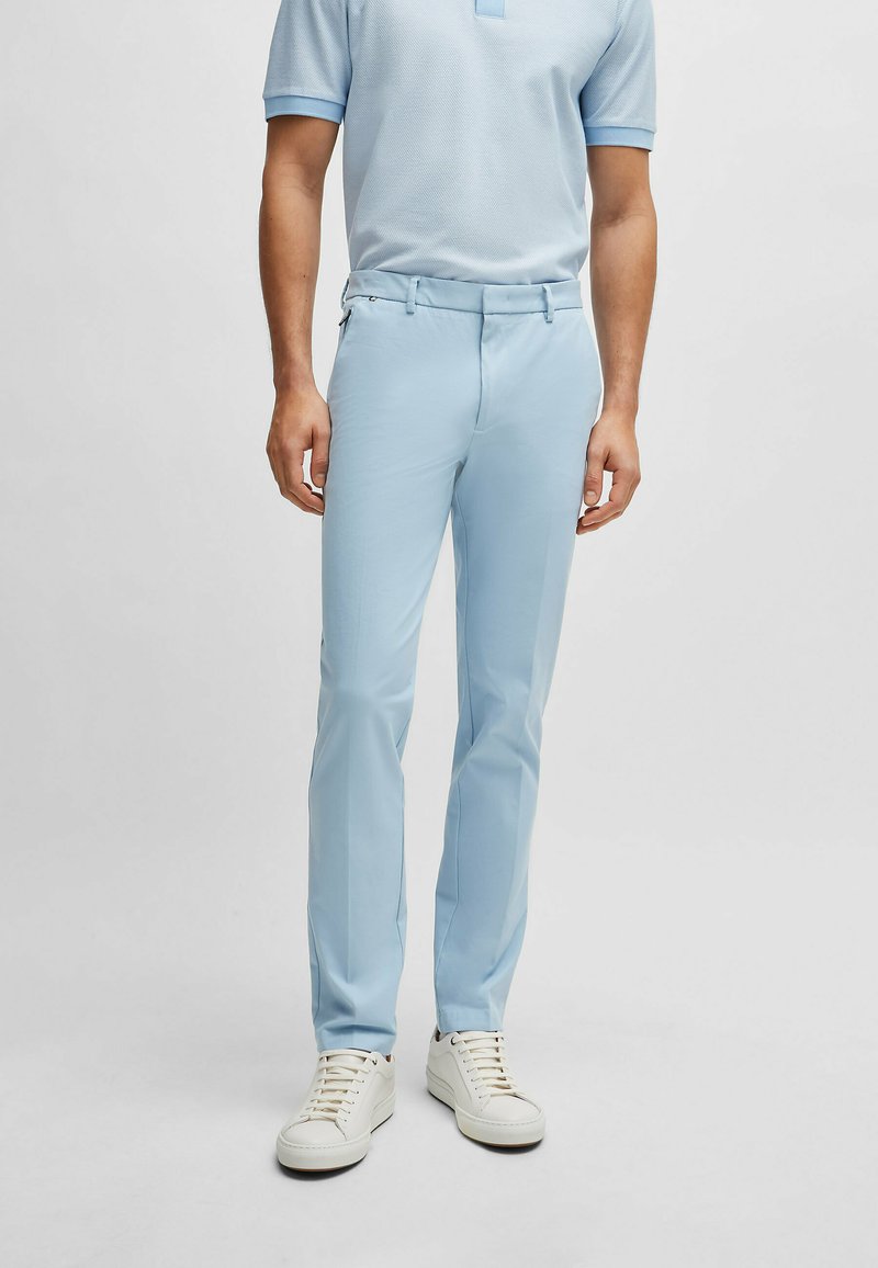 Light blue tailored trousers made of smooth fabric, featuring a zippered pocket and a straight-leg design, paired with white sneakers.