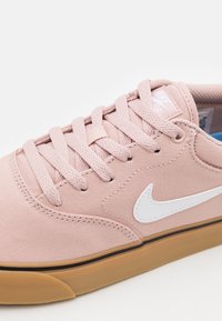 Rosa canvas sneakers med vit swoosh-logga, platta skosnören och gummisula. Har en vadderad krage och en texturerad yta.