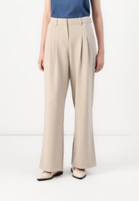 Beige wide-leg trousers with pleats, crafted from smooth fabric, feature a classic high waist. Paired with light-colored shoes.