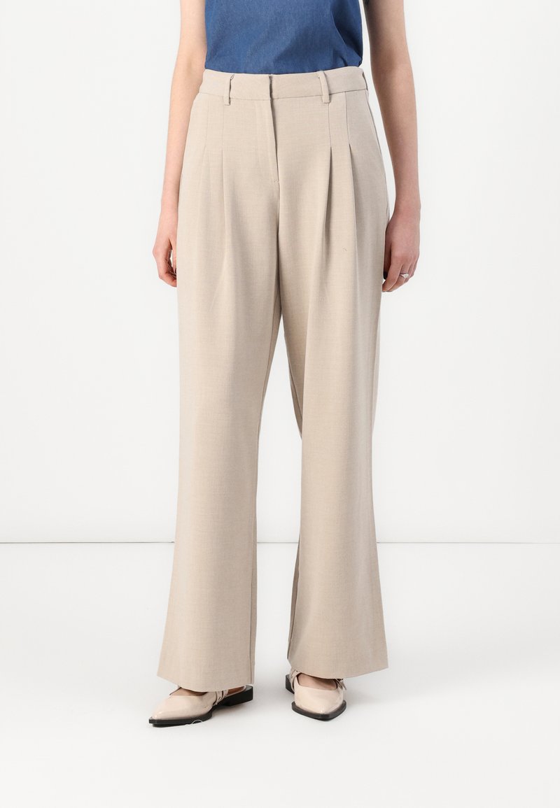 Beige wide-leg trousers with pleats, crafted from smooth fabric, feature a classic high waist. Paired with light-colored shoes.
