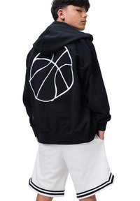 Felpa nera con una grafica di basket bianca sulla schiena, abbinata a pantaloni corti bianchi con dettagli a strisce nere.