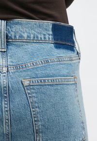 Pantalones vaqueros de mezclilla azul claro con una textura ligeramente desgastada, que cuentan con una cintura alta y dos bolsillos traseros con contornos cosidos.