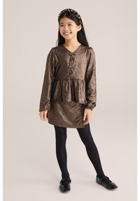 Brūns mirdzošs kleita ar garām piedurknēm, pepluma vidukli, V veida kakla izgriezumu un divām priekšējām lentēm. Uzvilkts kopā ar melnajām zeķēm un lakota ādas apaviem.