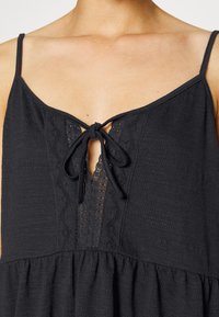 Vestido preto sem mangas com um detalhe de nó no pescoço, tecido texturizado, pormenores em renda e um corte solto com saia ampla.