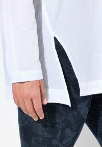 Witte shirt met een zijsplit detail, knoopmanchetten en van lichte, ademende stof. Gepaard met donkere, gebloemde denim.