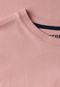 Camiseta de algodón rosa claro con escote redondo, con un fino ribete acanalado y una etiqueta azul marino en el cuello. Textura suave, diseño ajustado.