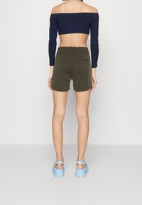 Pantaloni corti verde oliva con una vestibilità rilassata e una vita elastica. Top navy a spalle scoperte con costine. Sandali con piattaforma blu. Design minimalista.