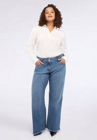 Blusa bianca con colletto abbinata a jeans blue a vita alta e gamba larga, con orlo sfrangiato e chiusura a bottone. Indossati scarpe nere con punta.