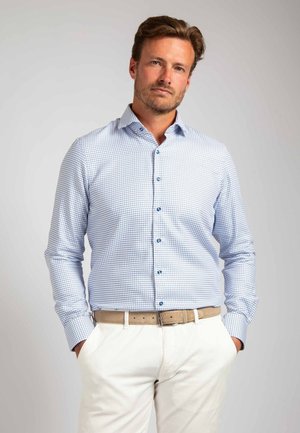 Lichtblauw geruit overhemd met lange mouwen en button-down kraag, gecombineerd met een beige riem en crèmekleurige broeken. Subtiele details bij de manchetten.