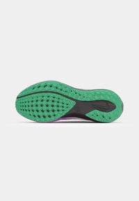 La suela del zapato Nike presenta un diseño de goma verde con patrones de agarre texturizados, delineado en negro y acentuado con púrpura en el borde del talón.