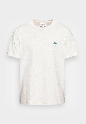 Biała koszulka z krótkim rękawem z delikatnymi wielokolorowymi kropkami i małym zielonym logo krokodyla Lacoste na lewej piersi.