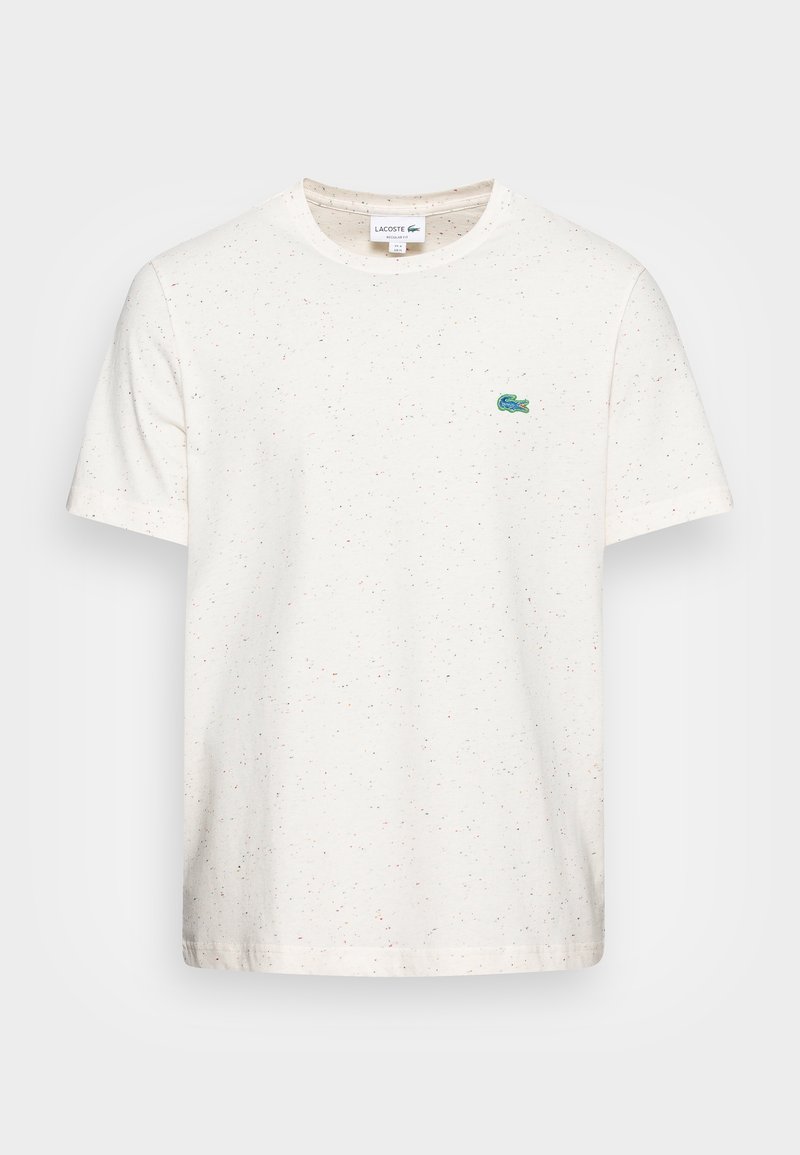 T-shirt blanc à manches courtes avec des petites taches multicolores discrètes et un petit logo crocodile Lacoste vert sur le côté gauche de la poitrine.