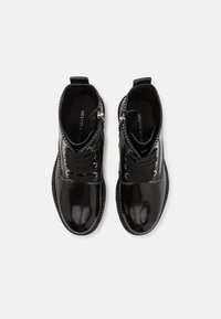 Paire de bottines en cuir noir brillant avec de gros lacets noirs, fermetures éclair latérales et coutures décoratives sur fond blanc.