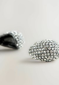 Agrafe de păr în formă ovală, decorate cu strasuri. Bază din metal argintiu cu o textură netedă, împodobită cu numeroase cristale strălucitoare.